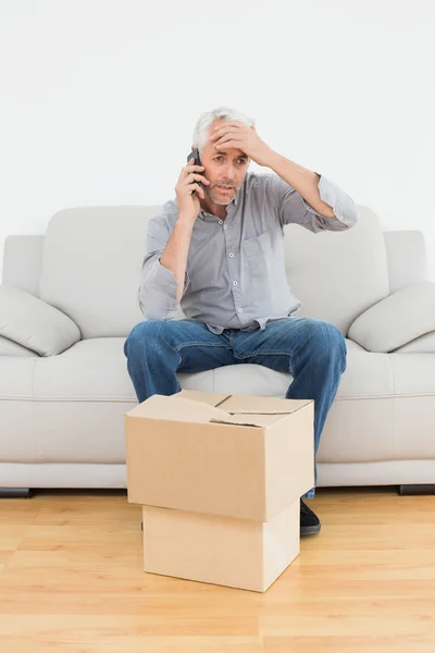 Hombre molesto usando cellpone en sofá con cajas en una casa nueva — Foto de Stock