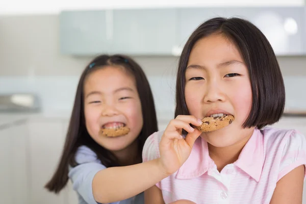 Girl feeding her elder sister a cookies in kitchen — Stock Photo, Image