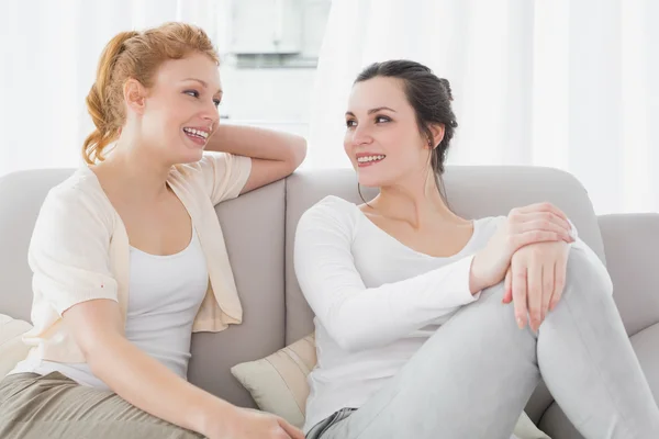 Två leende kvinnliga vänner sitter på soffan i vardagsrummet — Stockfoto