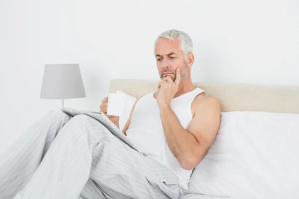 Człowiek z filiżanki kawy, czytanie gazety w łóżku — Zdjęcie stockowe