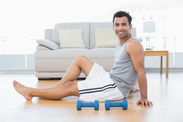 Relaxed man sitting on floor with dumbbells in the living room — Stock Photo, Image