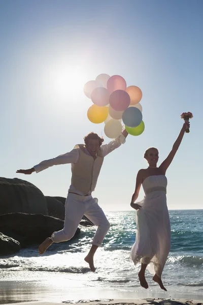 Groom holding balloons and bride throwing her bouquet jumping — Stock Photo, Image