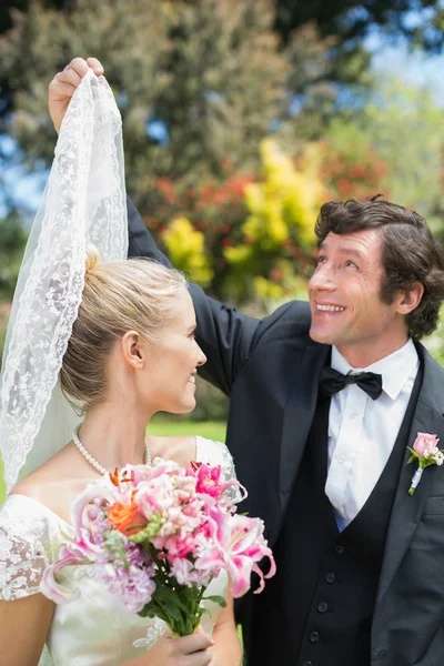 Groom holding his wifes veil smiling at each other — Stock Photo, Image