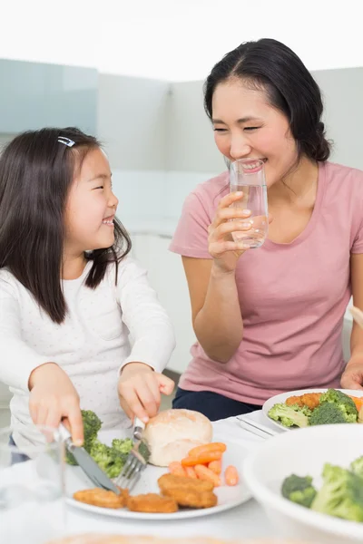 Mother watching little girl eat food in kitchen — Stock Photo, Image