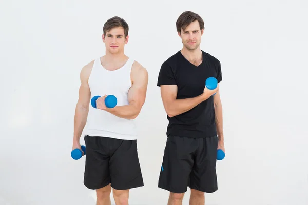 Портрет двух молодых людей, сгибающих мышцы гантелями — стоковое фото