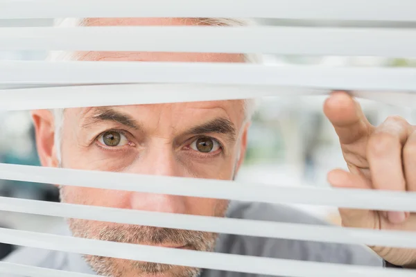 Close-up of a mature businessman peeking through blinds — Stock Photo, Image