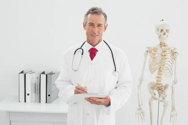 Médico varón sonriente escribiendo un informe en el consultorio — Foto de Stock