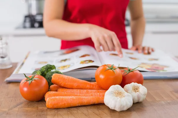 Mitten delen av en kvinna med receptbok och grönsaker i kök — Stockfoto