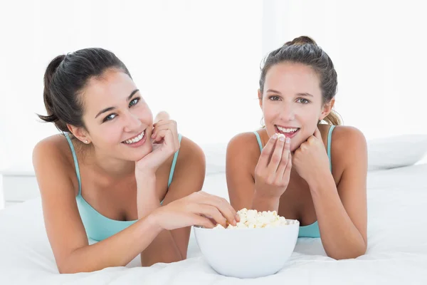 Smiling female friends eating popcorn in bed — Stock Photo, Image