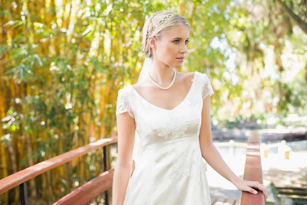 Content blonde bride in pearl necklace standing on a bridge — Stock Photo, Image