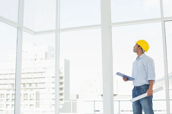 Handyman in hard hat with clipboard and blueprint looking at window