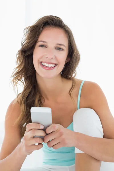 Mujer joven sonriente con teléfono móvil en la cama —  Fotos de Stock