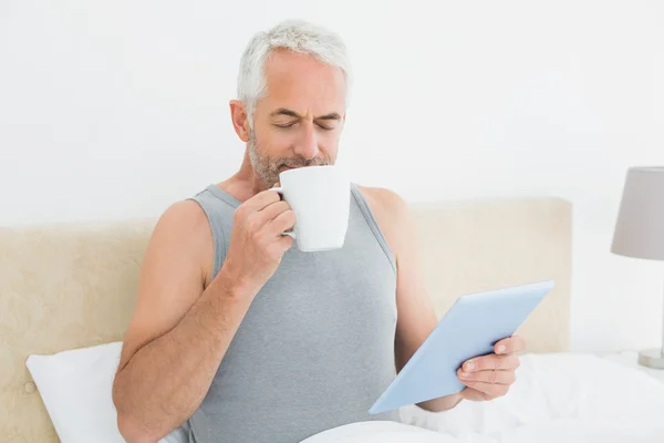 Mann mit digitalem Tablet trinkt Kaffee im Bett — Stockfoto