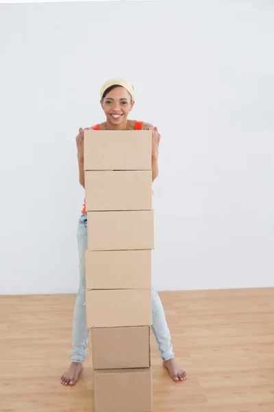 Smiling woman moving in a new house with a stack of boxes — Stock Photo, Image