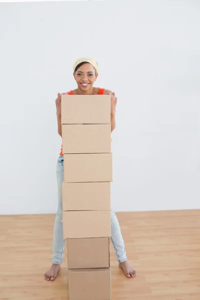 Mujer sonriente moviéndose en una casa nueva con una pila de cajas — Foto de Stock