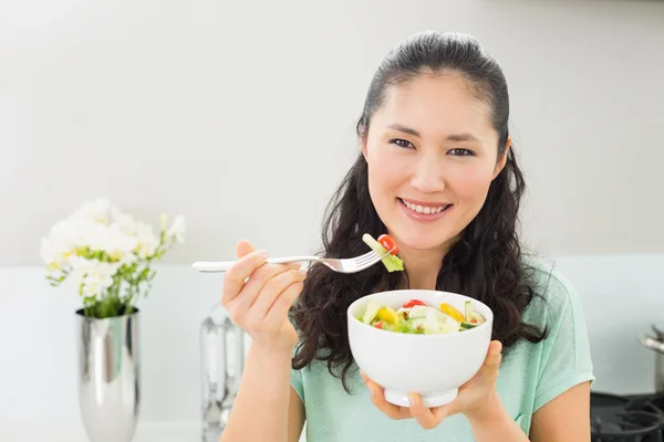 Jonge vrouw met een kom van salade in keuken glimlachen — Stockfoto