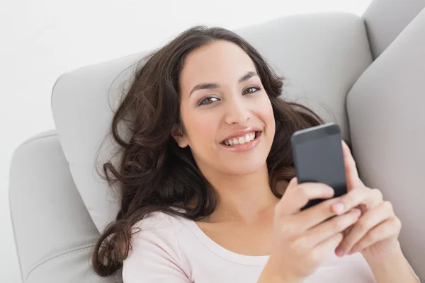 Sorridente messaggio di testo giovane donna sul divano a casa — Foto Stock