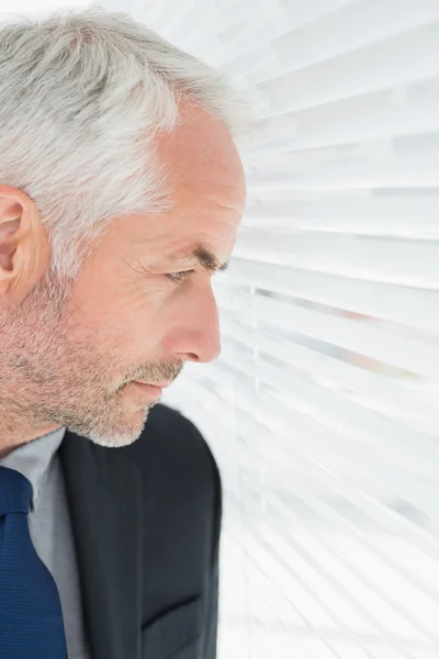 Ernstige volwassen zakenman gluren via blinds in office — Stockfoto