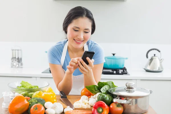 Woman text messaging in front of vegetables in kitchen — Stock Photo, Image