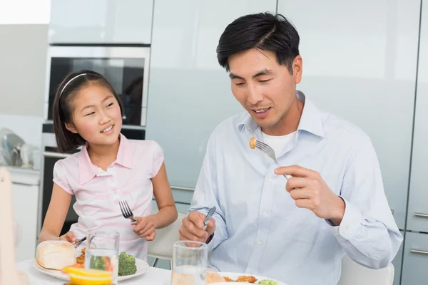 小女孩看着父亲用叉子在厨房里吃的食物 — 图库照片