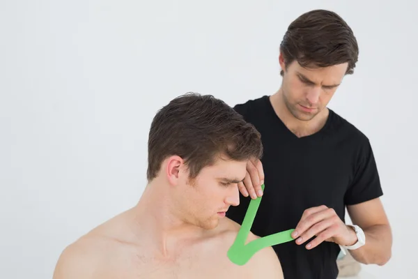 Физиотерапевт надевает кинезиоленту на плечо пациента — стоковое фото