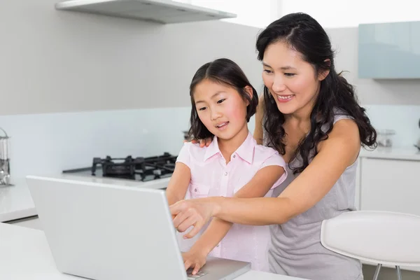 Sonriente madre con hija joven utilizando el ordenador portátil en la cocina —  Fotos de Stock