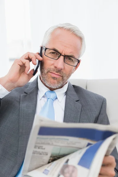 Ernstige zakenman met mobiel en krant thuis — Stockfoto