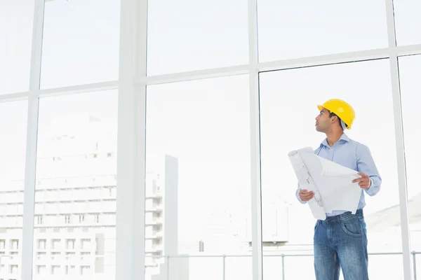 Architect in yellow hard hat with plans looking up at window — Stock Photo, Image
