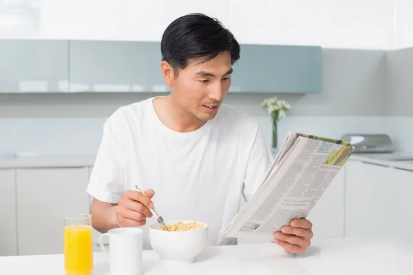 Jonge man met granen tijdens het lezen van de krant in keuken — Stockfoto