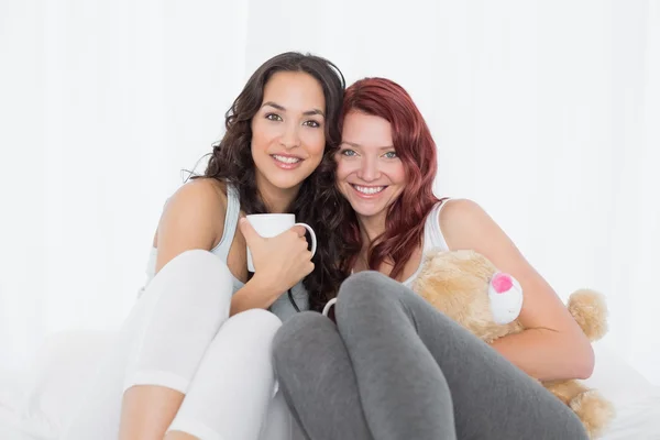 Happy young female friends with coffee cups in bed — Stock Photo, Image