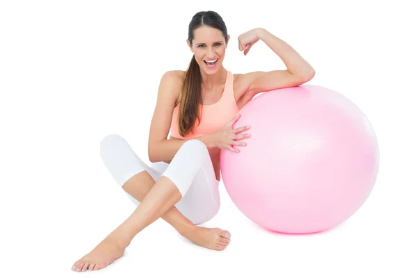 Mulher apto alegre flexionando músculos por bola de fitness — Fotografia de Stock