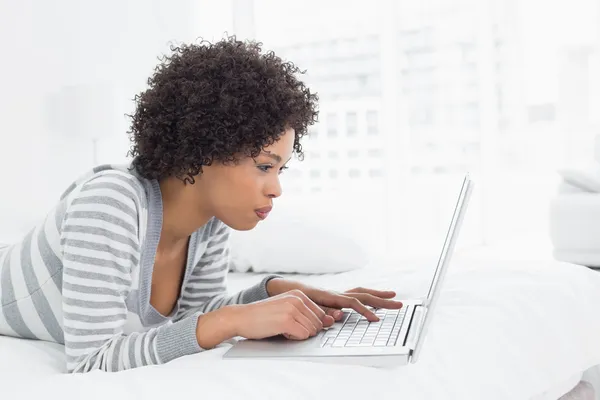 Serious young woman using laptop in bed — Stock Photo, Image