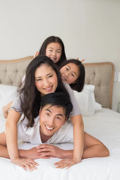 Alegre familia de cuatro acostados uno sobre el otro en la cama —  Fotos de Stock