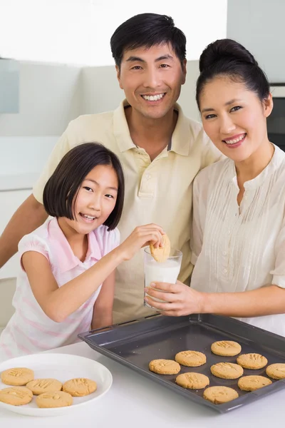 Meisje genieten van cookies en melk met ouders in keuken — Stockfoto