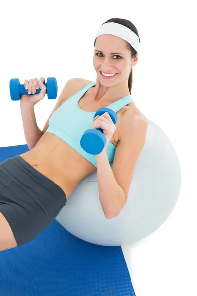 Mujer sonriente en forma haciendo ejercicio con pesas en la pelota de fitness —  Fotos de Stock