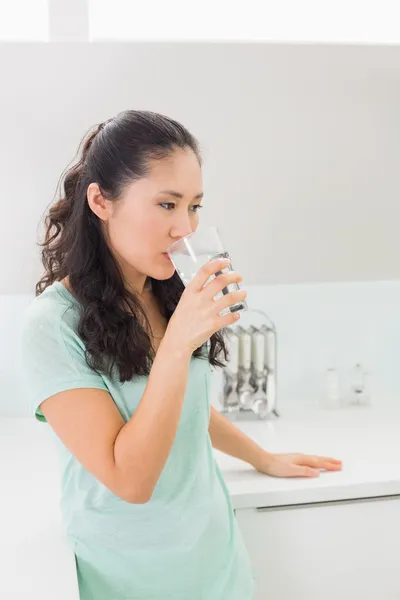 Giovane donna che beve acqua in cucina — Foto Stock