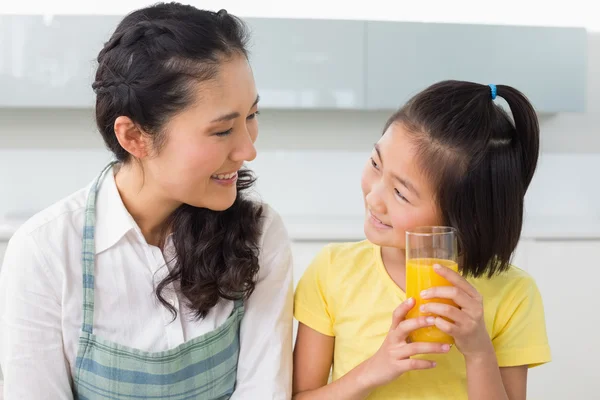 Ung flicka håller apelsinjuice med sin mamma i köket — Stockfoto