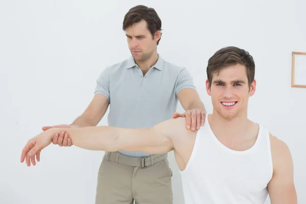 Fisioterapeuta masculino examinando un brazo de hombre joven — Foto de Stock