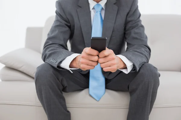 Mid section of a well dressed man text messaging on sofa — Stock Photo, Image