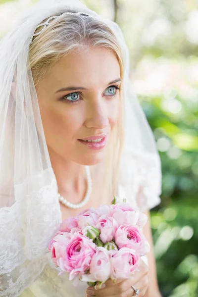 Contenuto sposa indossa velo tenendo bouquet guardando altrove — Foto Stock