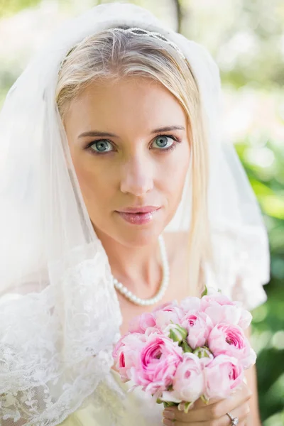 Felice sposa in un velo che tiene il suo bouquet guardando la fotocamera — Foto Stock