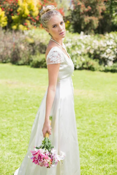 Beautiful blonde bride holding bouquet looking away — Stock Photo, Image