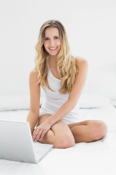 Lächelnde junge Frau sitzt mit Laptop auf dem Bett — Stockfoto