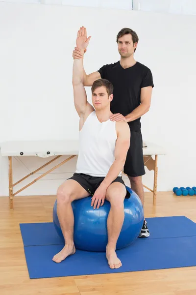 Человек на мяче для йоги работает с физиотерапевтом — стоковое фото