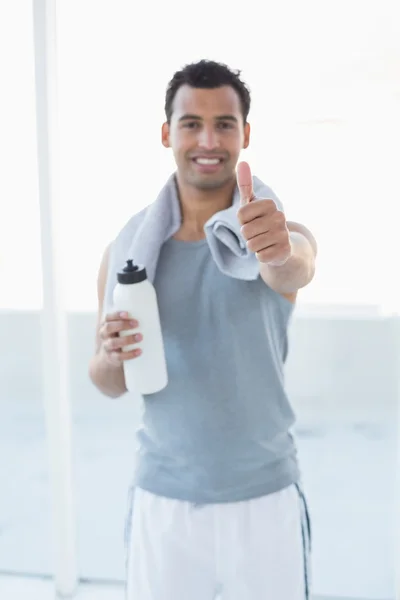 Uomo con bottiglia d'acqua e asciugamano gesticolando pollici in alto in palestra — Foto Stock