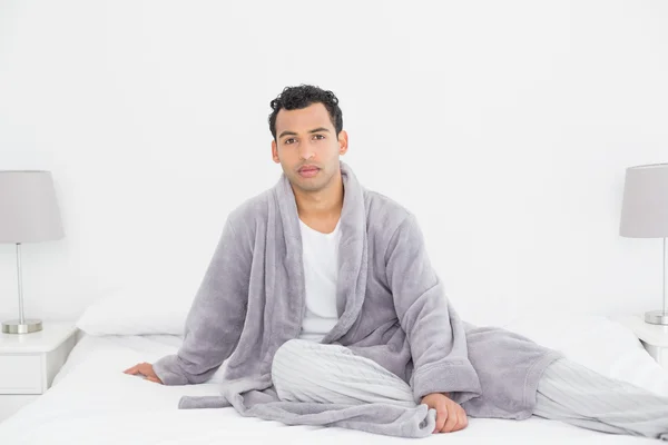 Entspannter junger Mann im Bademantel sitzt auf Bett — Stockfoto