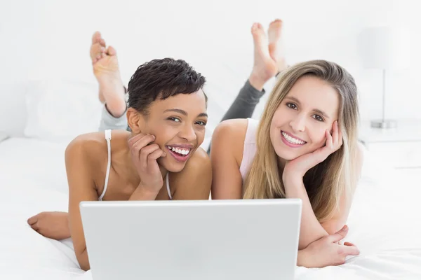 Relajado jóvenes amigas utilizando el ordenador portátil en la cama —  Fotos de Stock