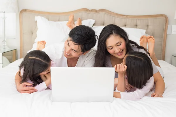 Familia feliz de cuatro usando portátil en la cama — Foto de Stock