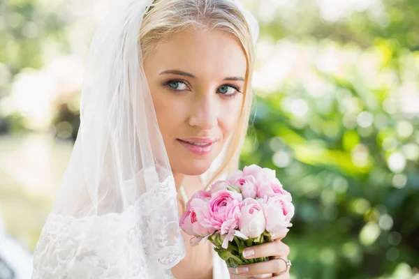 Lächelnde Braut mit Schleier über dem Gesicht hält Strauß in die Kamera — Stockfoto