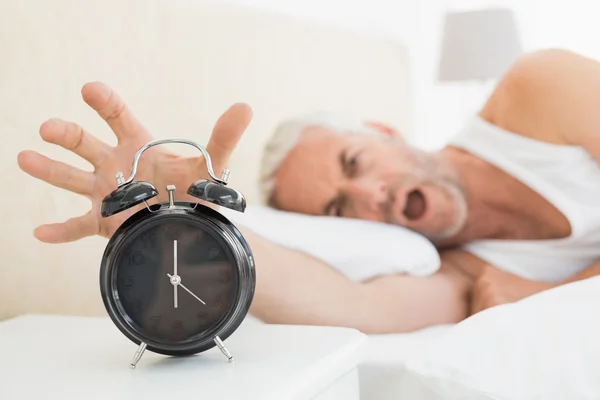 Blurred mature man extending hand to alarm clock — Stock Photo, Image